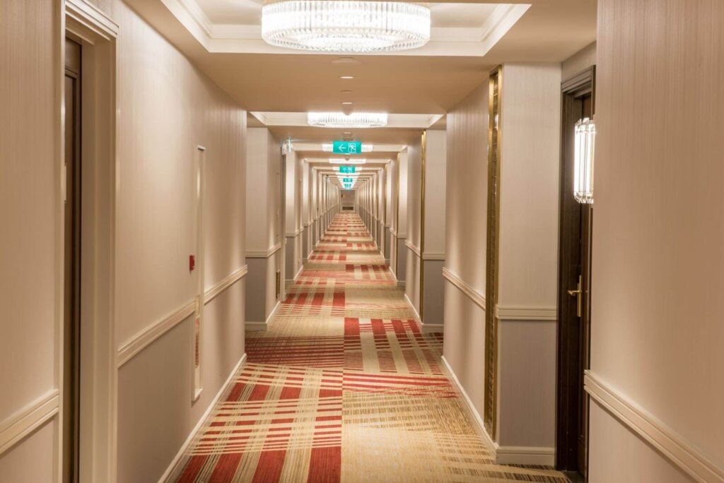 A carpeted hotel corridor with an acoustical ceiling